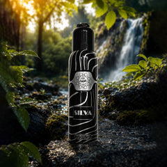 A black cylindrical bottle labeled 'SILVA' and 'Agath' stands on a mossy rock in a forest with a waterfall in the background. The bottle has a glossy black finish with silver abstract line patterns and a silver label.