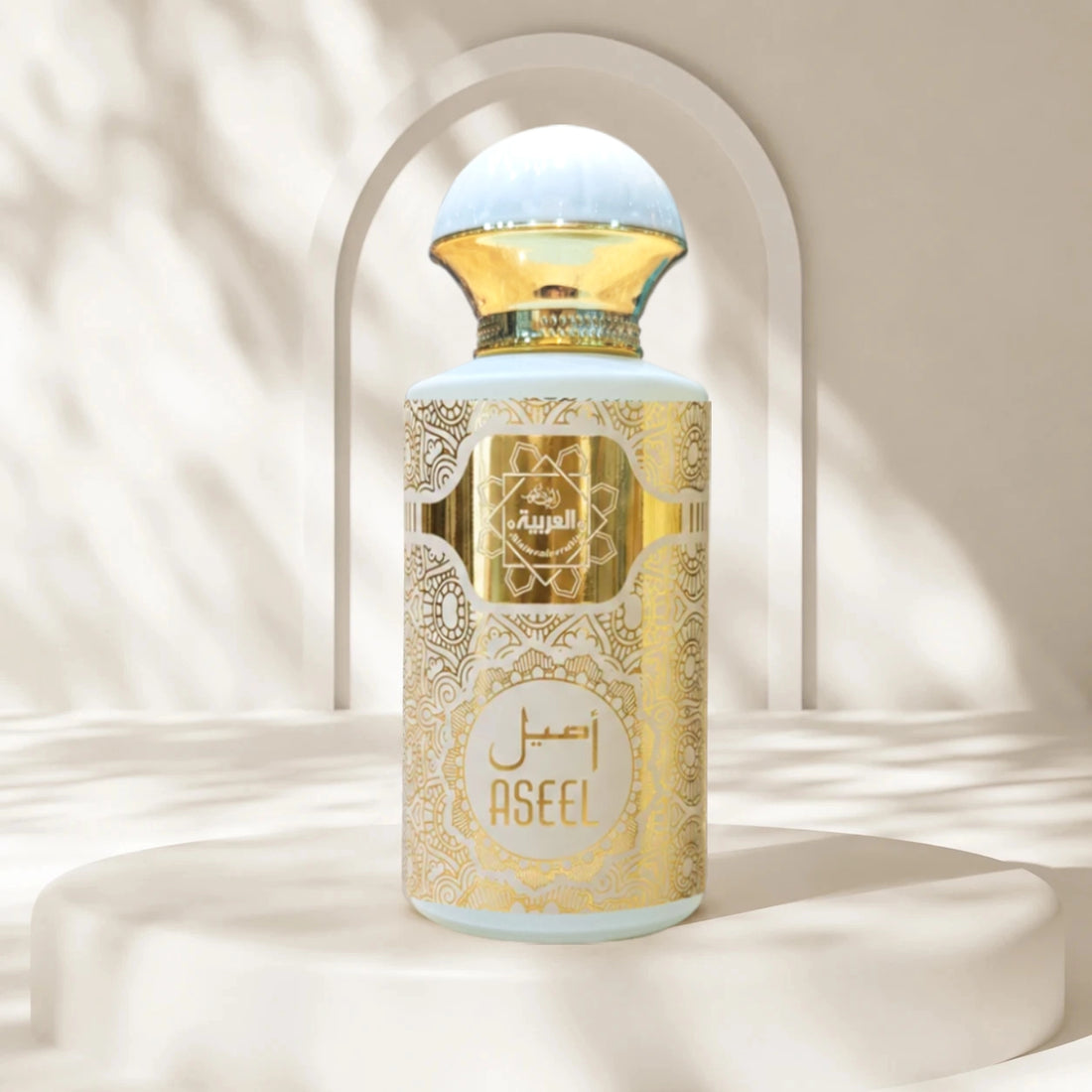 A perfume bottle labeled ASEEL by Al Rajai, featuring a light blue body with ornate gold patterns and a gold cap, displayed on a white pedestal with soft shadow overlays.