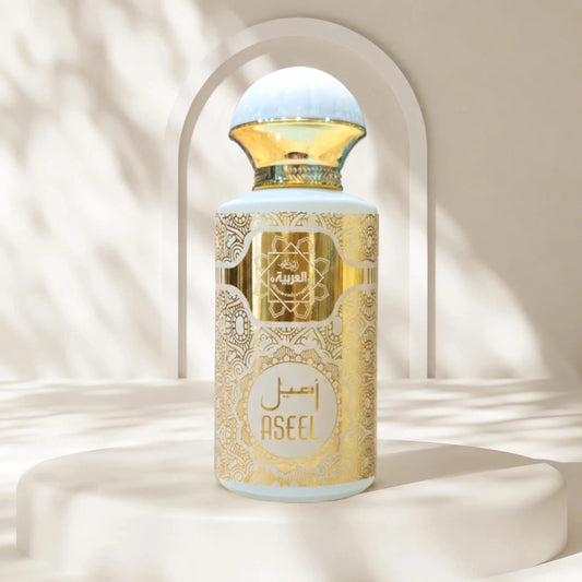 A perfume bottle labeled ASEEL by Al Rajai, featuring a light blue body with ornate gold patterns and a gold cap, displayed on a white pedestal with soft shadow overlays.